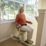 Happy elderly woman on a stair lift after getting home safety upgrades in Canton, MI